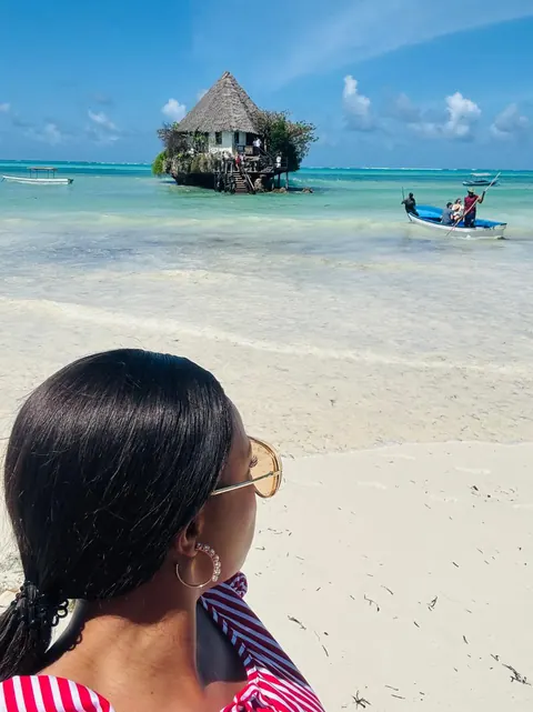 A traveller on the beach looking towards a thatched restaurant on a rock