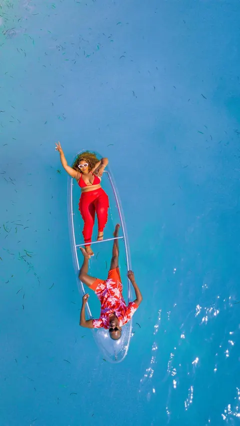 Two travellers relaxing in a transparent kayak above clear blue water